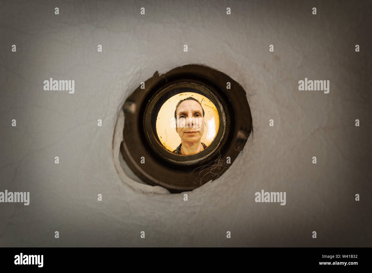 Woman seen out of focus through the old dirty peephole of the front door of a dark apartment Stock Photo