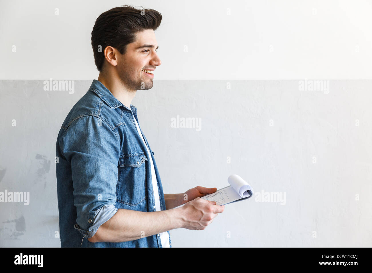 Attractive young man standing at the kitchen at home, holding clipboard, working Stock Photo