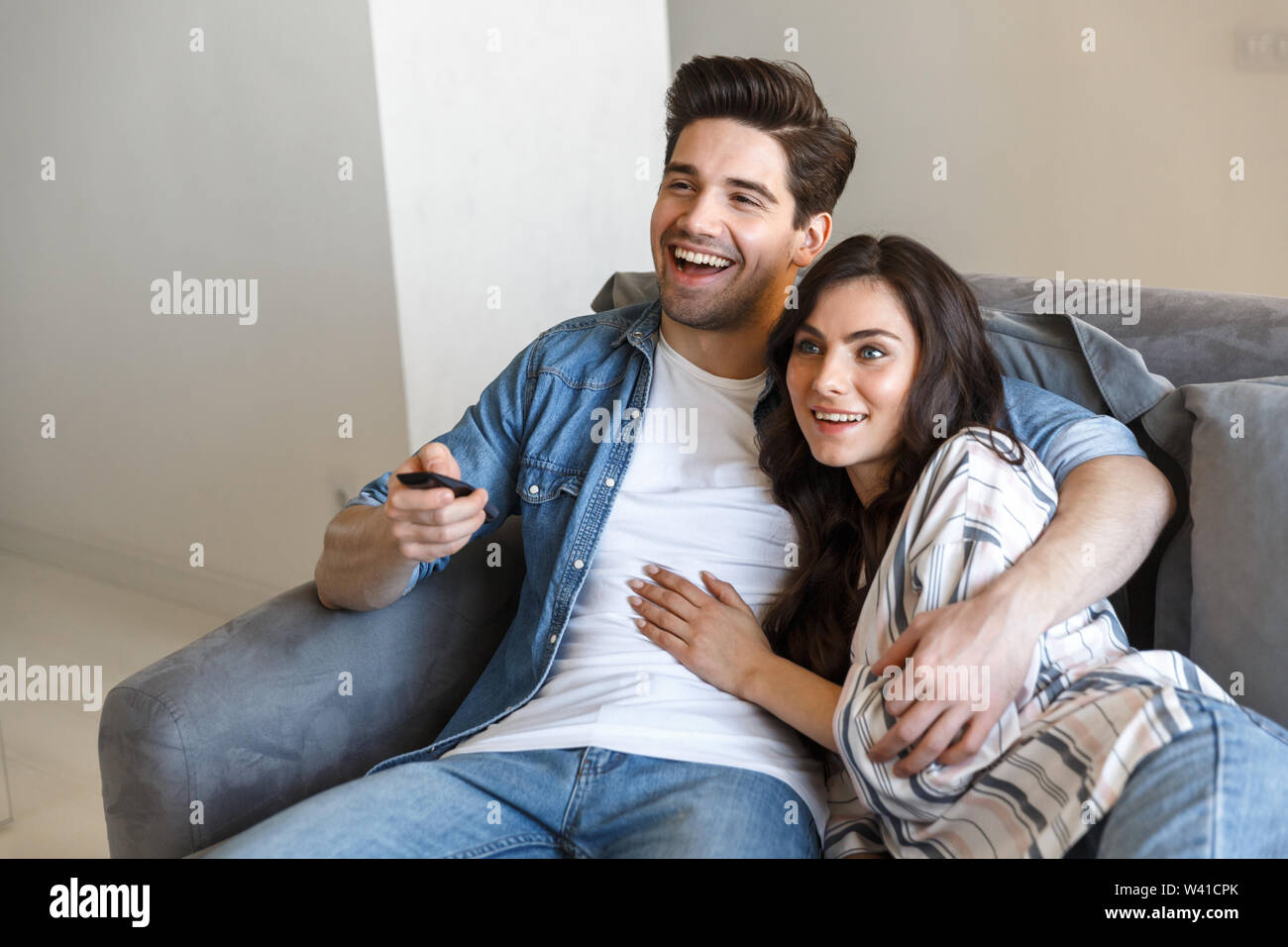 Attractive Young Couple Relaxing On A Couch At Home Watching Tv