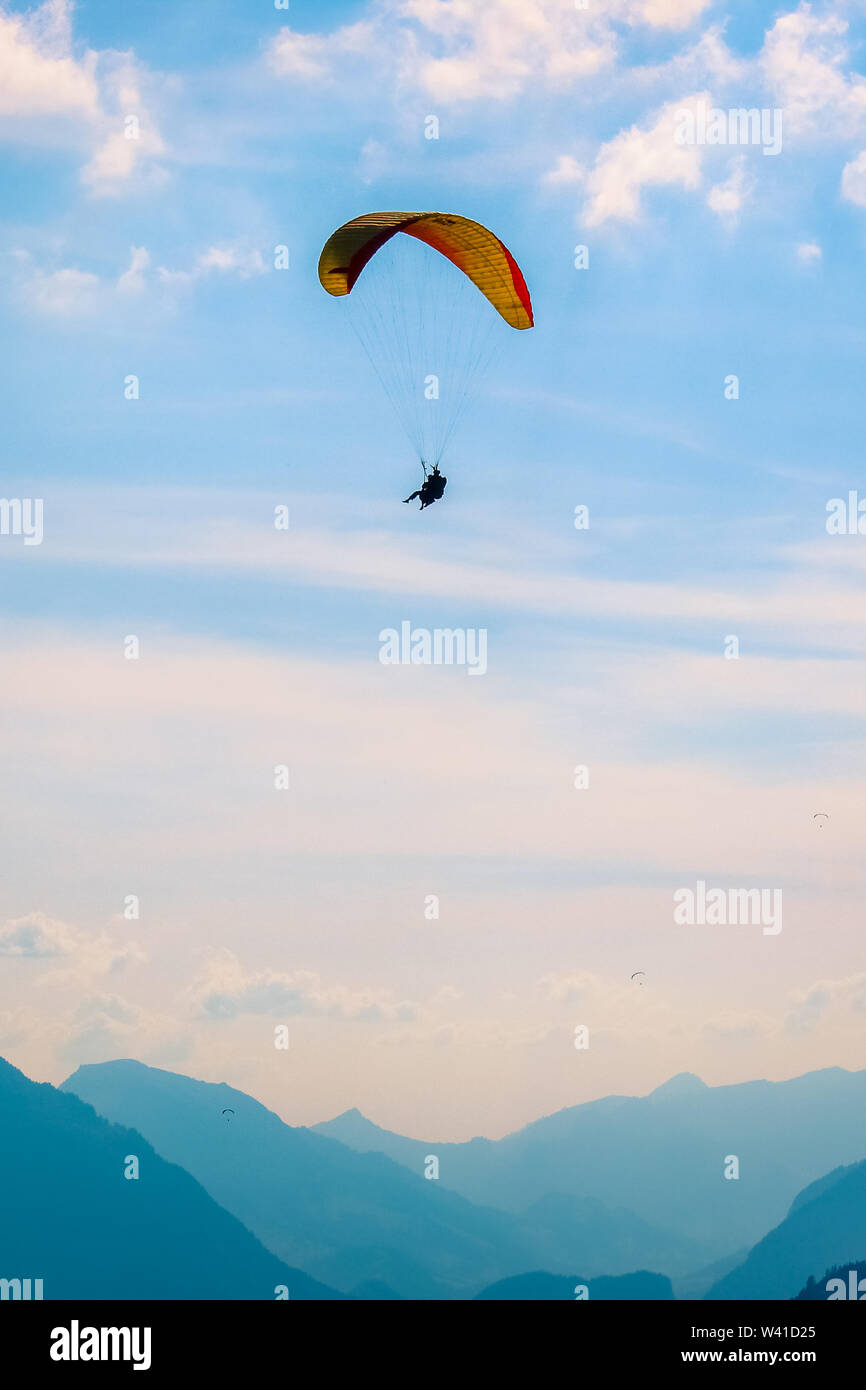 Tandem paragliding over Swiss Alps in sunset light. Photographed in Interlaken, Switzerland. Silhouettes of Swiss Alps and paragliders. Adventure sports, extreme. Adrenaline activities. Conceptual. Stock Photo