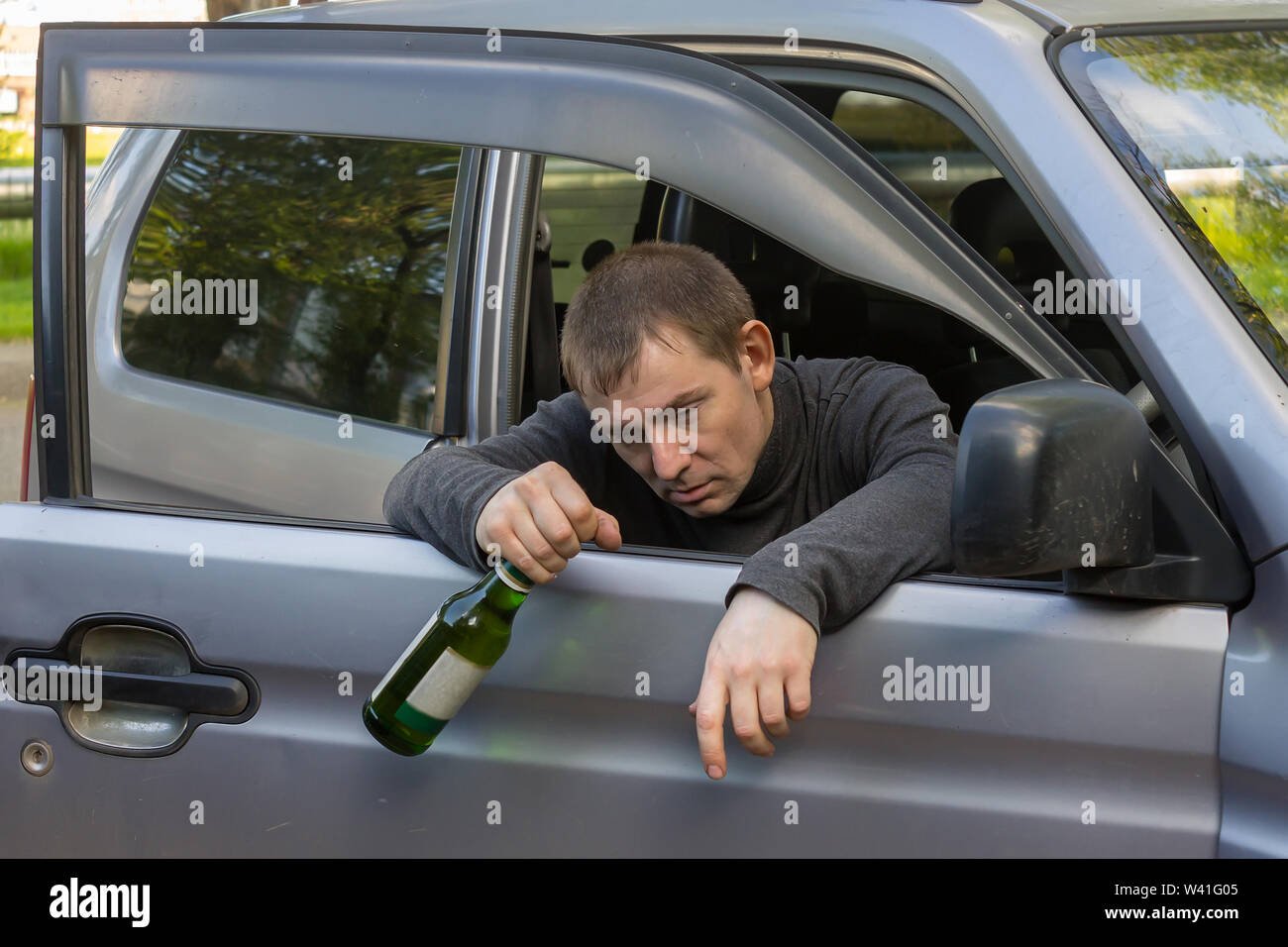 Drunk and irresponsible driver hanging on the doors of his car with a  bottle of alcoholic beverage Stock Photo - Alamy