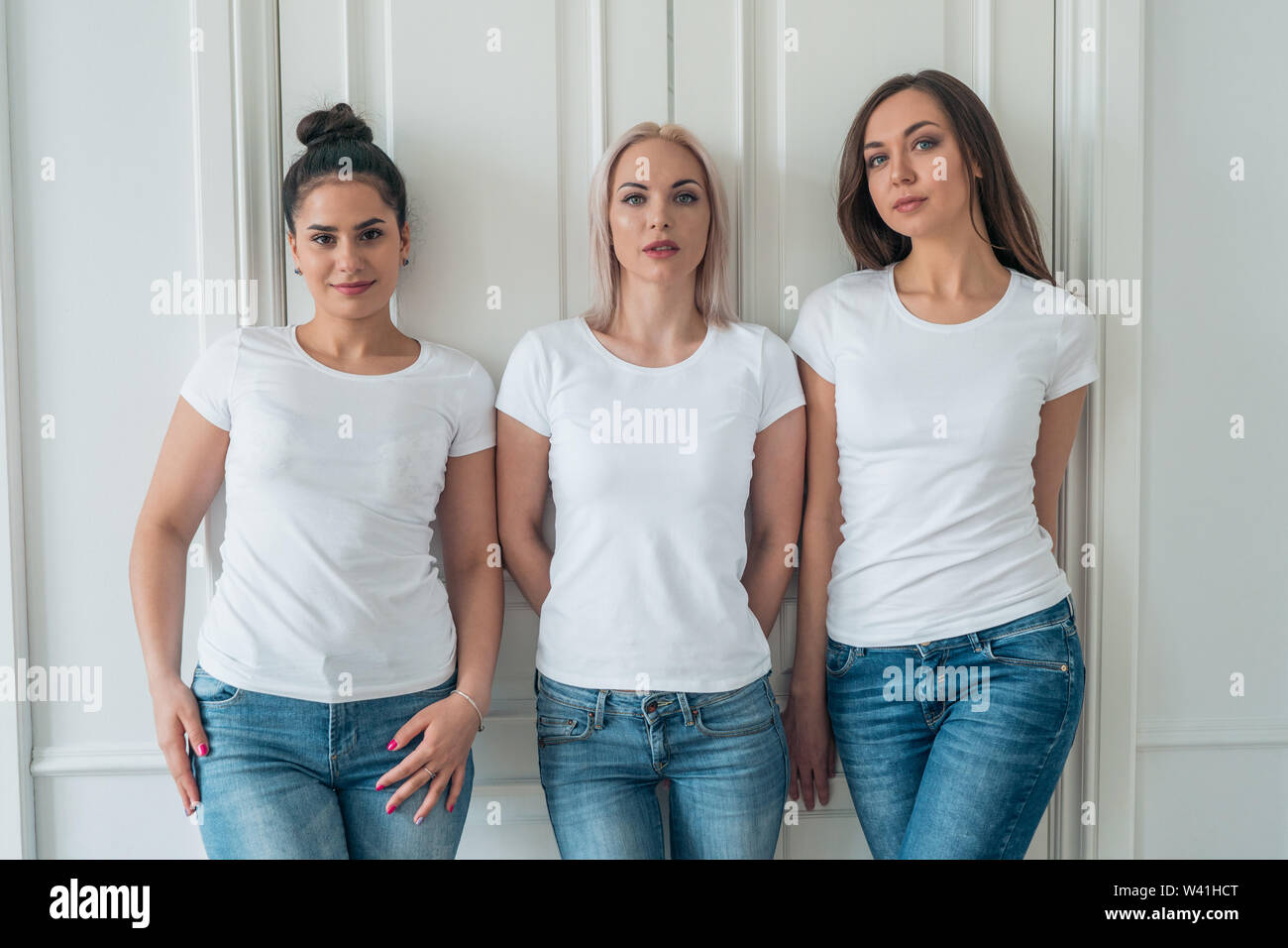 Three beautiful girls models posing in white T-shirts and blue jeans. Layout for design on t-shirts Stock Photo