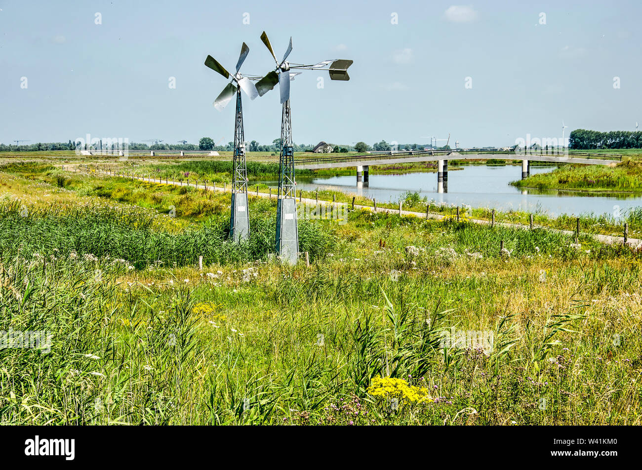 Landscape in the Noordwaard section of Biesbosch national park in the Netherlands, with two small steel windmills, a cycle path, a creek and a bridge Stock Photo