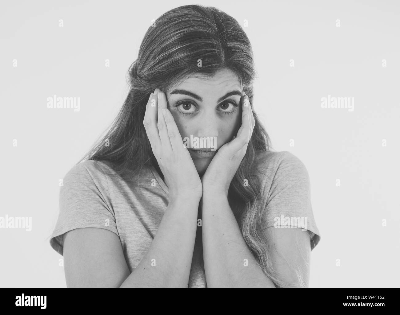 Close up in black and white of young woman feeling afraid and shocked hiding her face from something scary. Looking with fear in her eyes. People and Stock Photo