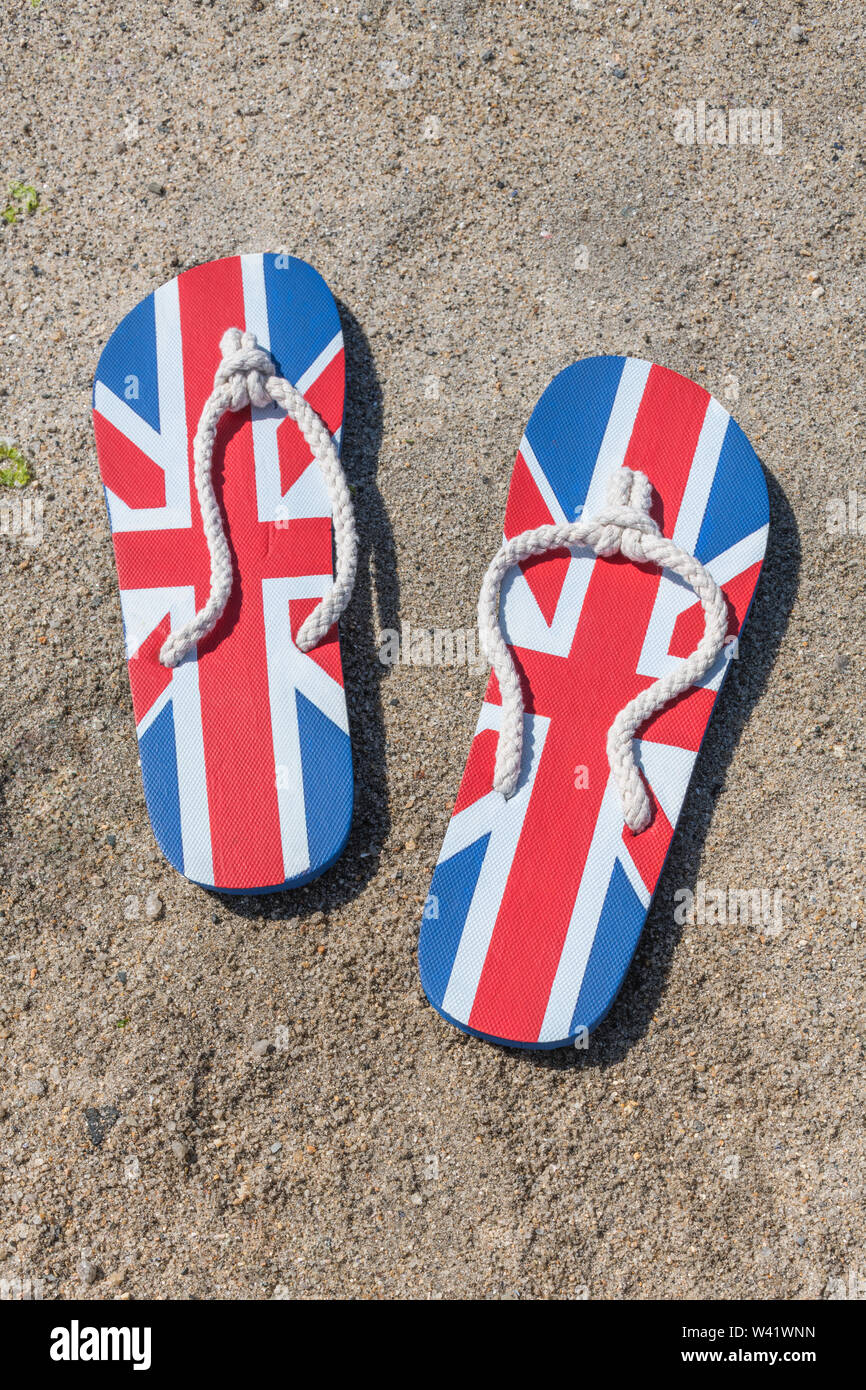 GB flag / Union Jack flip-flops on sandy beach - for 2021 UK staycation, holidays at home, staycation Cornwall, seaside holiday, flip-flop footwear. Stock Photo