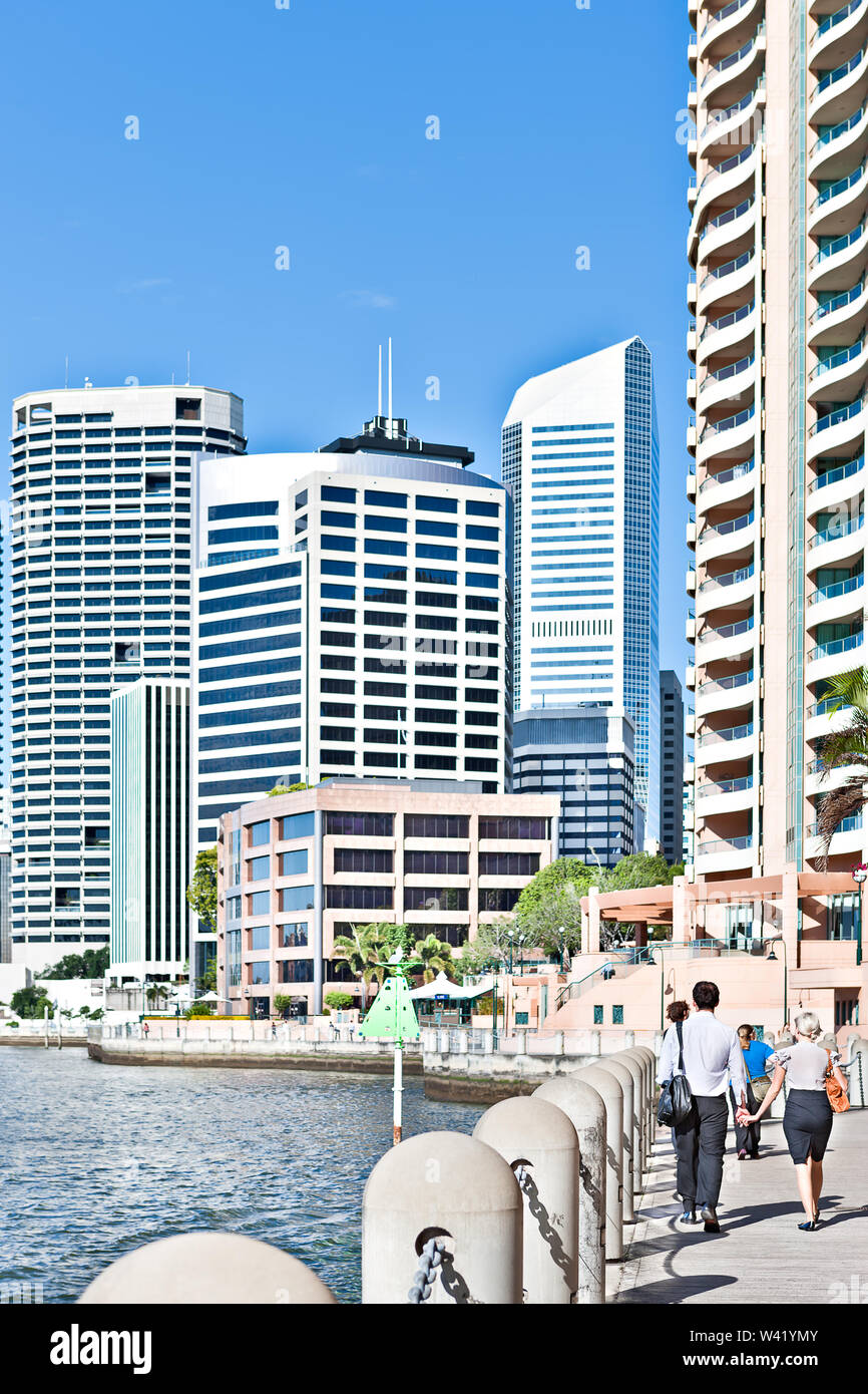 People are walking on the street of a modern city's waterside near to the river and into the huge buildings with blue sky Stock Photo