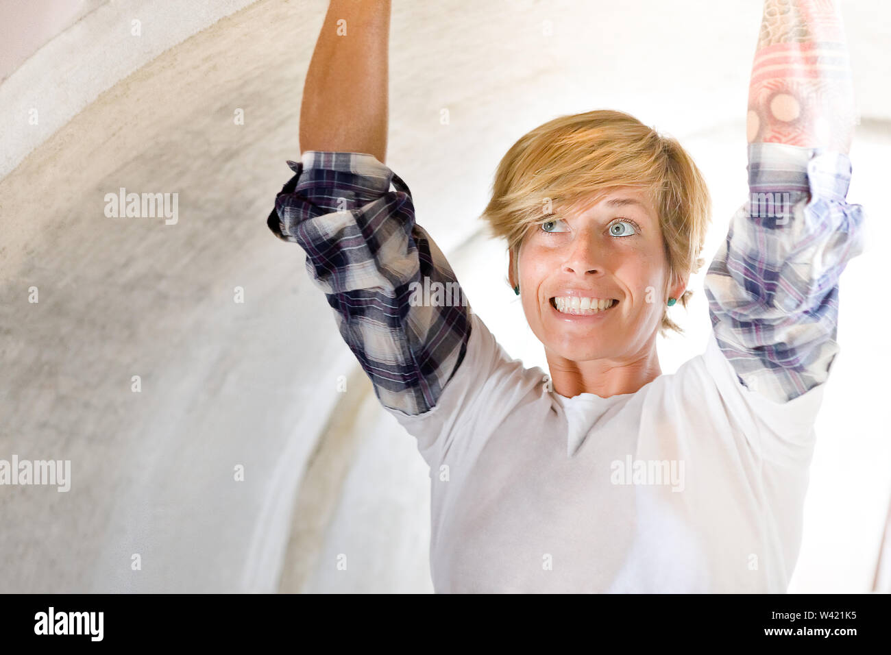 Gold and short haired girl touching the inside of a concrete pipe with her tattooed hands  and laughing Stock Photo