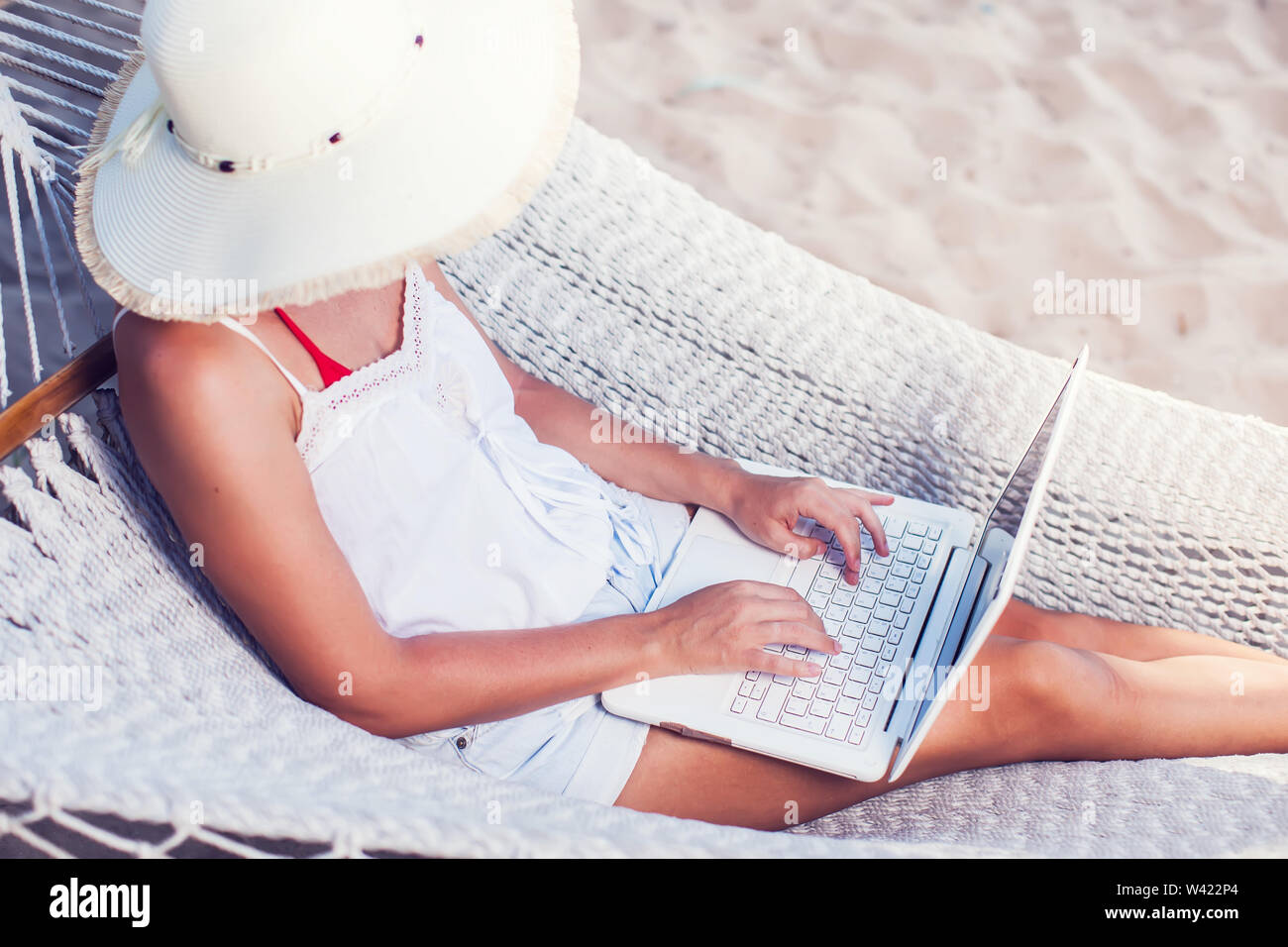 Woman using her laptop in hammock on the beach Stock Photo