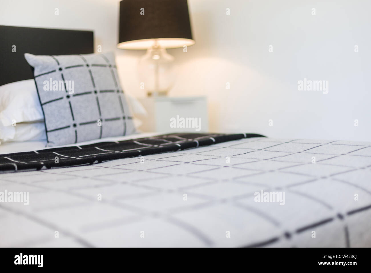 A view of a double bed with a single pillow kept on it featuring box design  and a lamp shade kept in background Stock Photo - Alamy