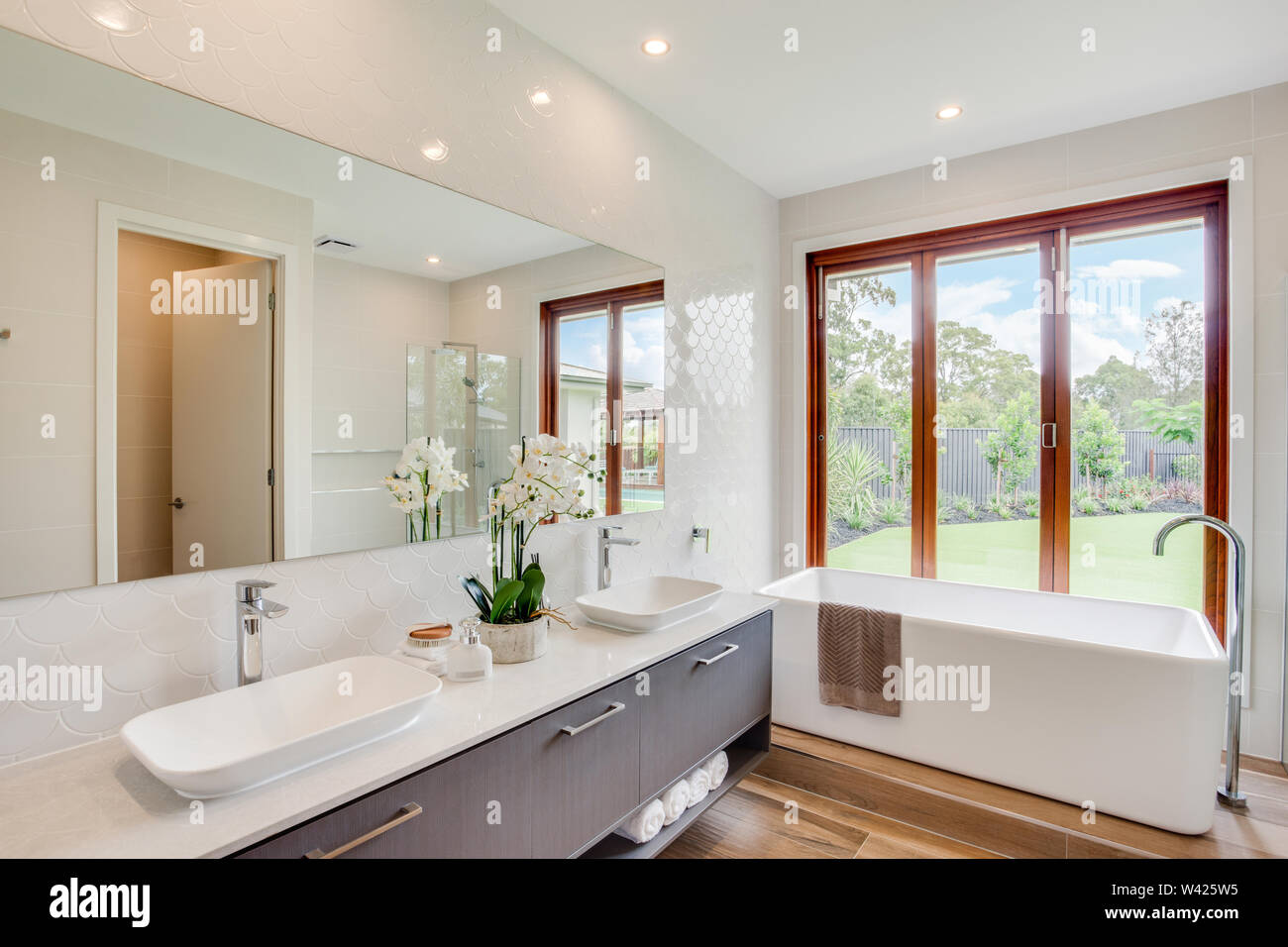 Bath tub adjacent to a dual sink counter, with windows facing the lawn