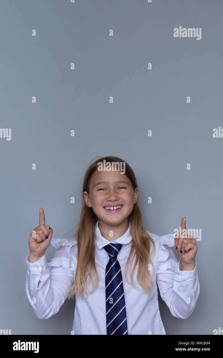 Young schoolchild pointing up portrait. Preteen schoolgirl looking at camera, gesturing at ceiling. Happy girl, kid in school uniform. Back to school, joyful, cheerful pupil, student ready for class Stock Photo