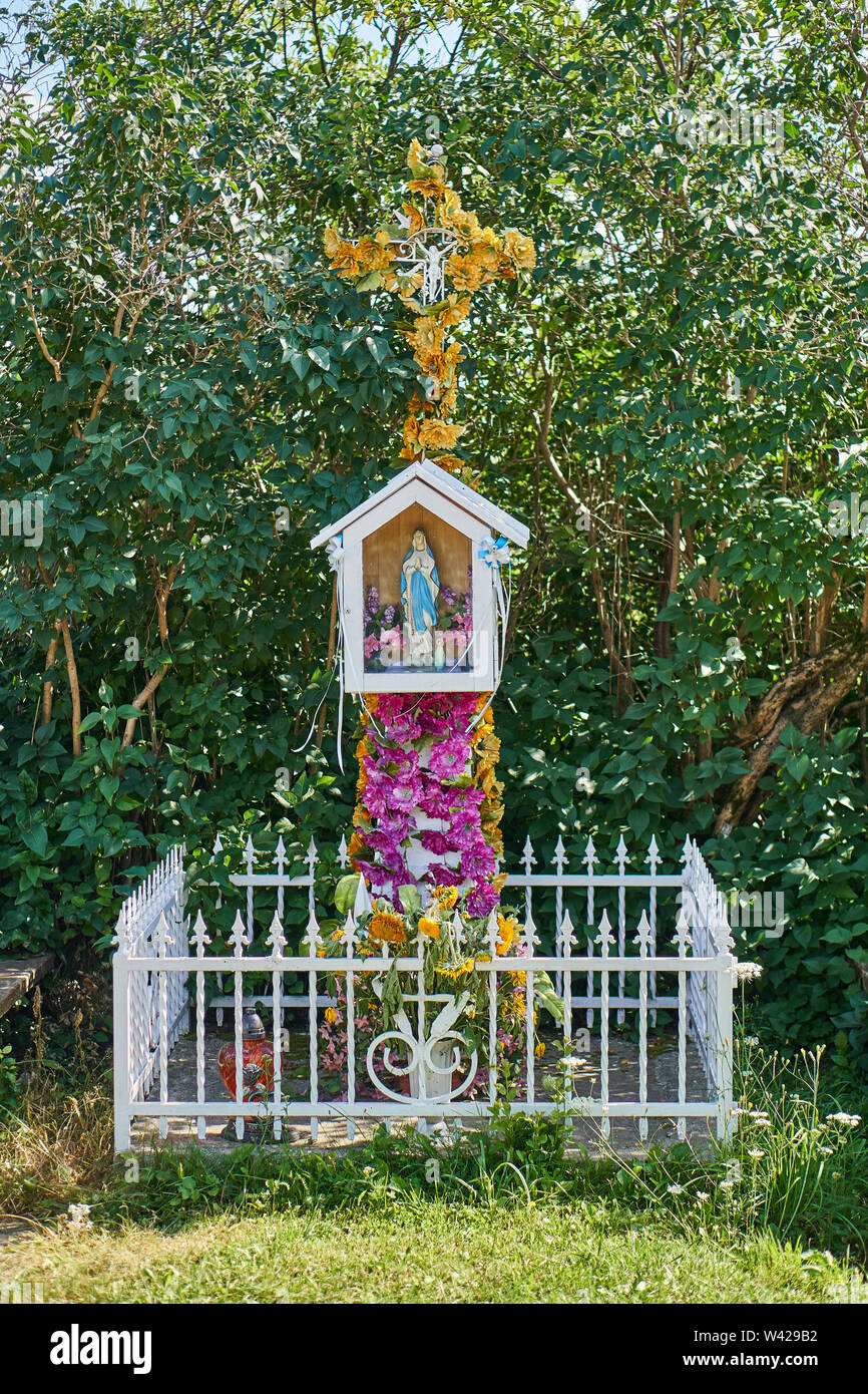 Traditional Catholic cachapel near the road in the shape of a cross with plastic artificial flowers, Biale, Poland Stock Photo