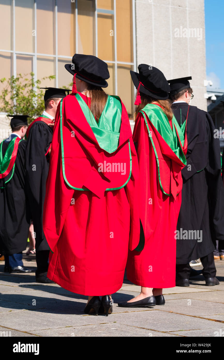 Higher education in the UK - two women successful PhD doctoral students at  the graduation ceremony at Aberystwyth university, after receiving their  degrees, wearing their traditional tudor style bonnet caps and red