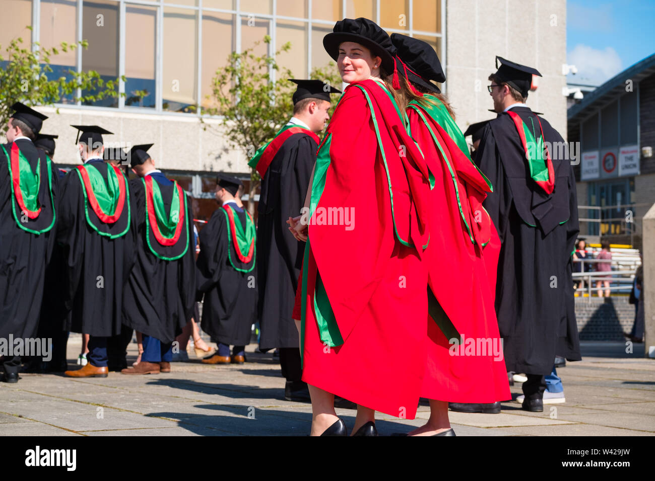 Higher education in the UK - two women successful PhD doctoral students at the graduation ceremony at Aberystwyth university, after receiving their degrees,  wearing their traditional tudor style bonnet caps and  red coloured  gowns. July 2019 Stock Photo