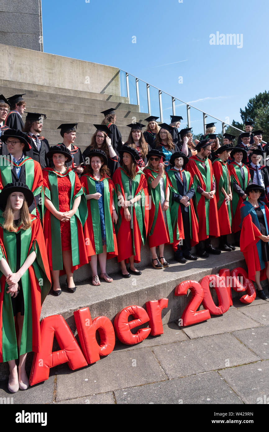 Higher education in the UK - successful PhD doctoral students at the graduation ceremony at Aberystwyth university, after receiving their degrees,  wearing their traditional tudor style bonnet caps and  red coloured  gowns. July 2019 Stock Photo