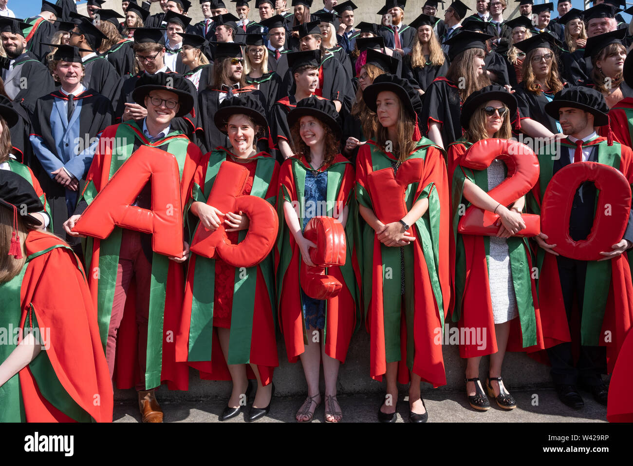 Higher education in the UK - successful PhD doctoral students at the graduation ceremony at Aberystwyth university, after receiving their degrees,  wearing their traditional tudor style bonnet caps and  red coloured  gowns. July 2019 Stock Photo