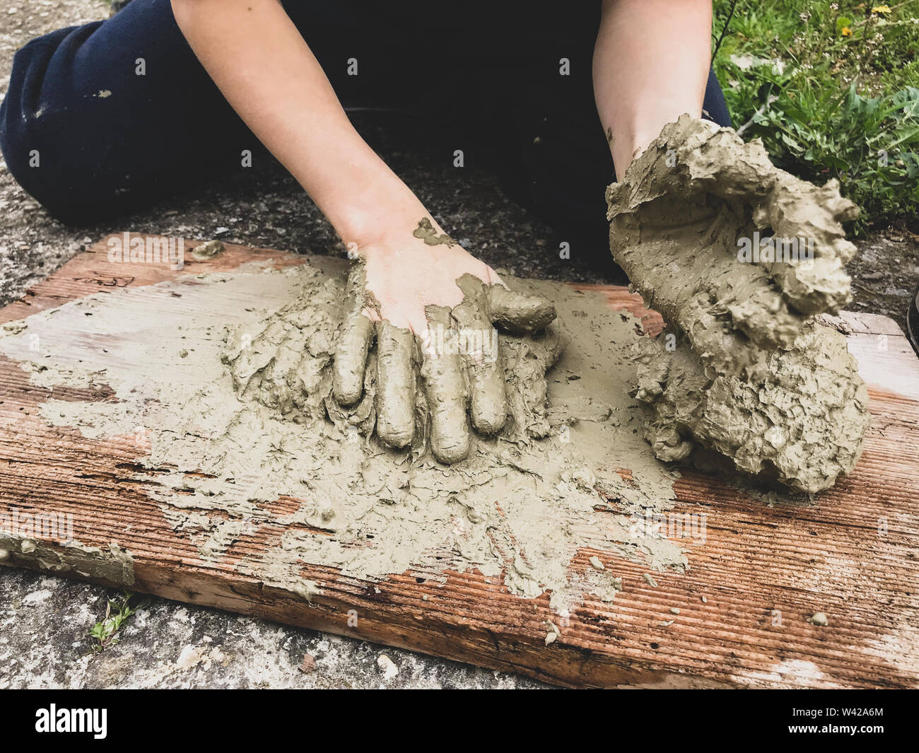 A kid kneads and models wet clay on a wooden plank on the floor Stock Photo