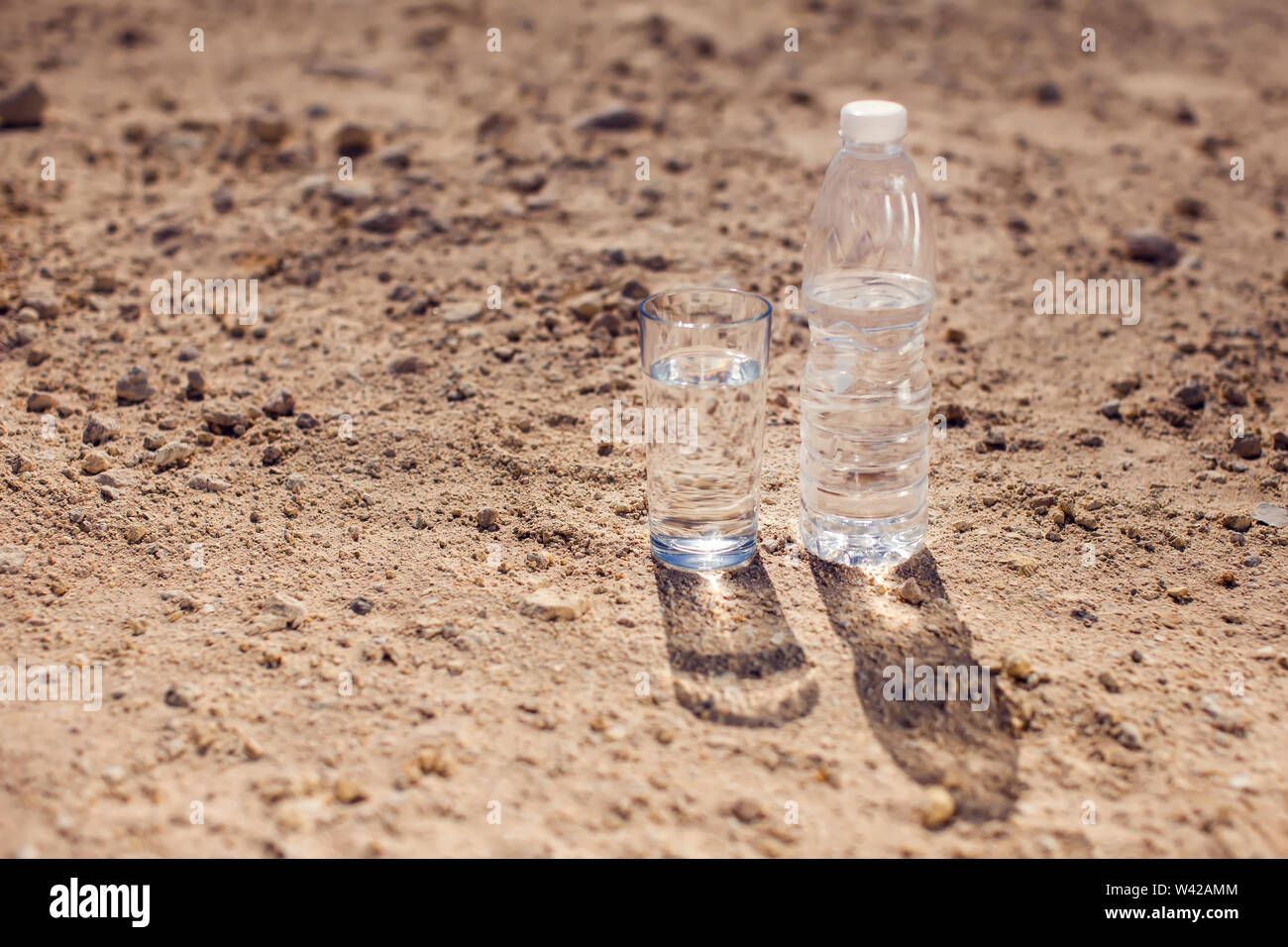Glass and bottle of water on sand in the desert. Thirsty, heat and drought concept Stock Photo