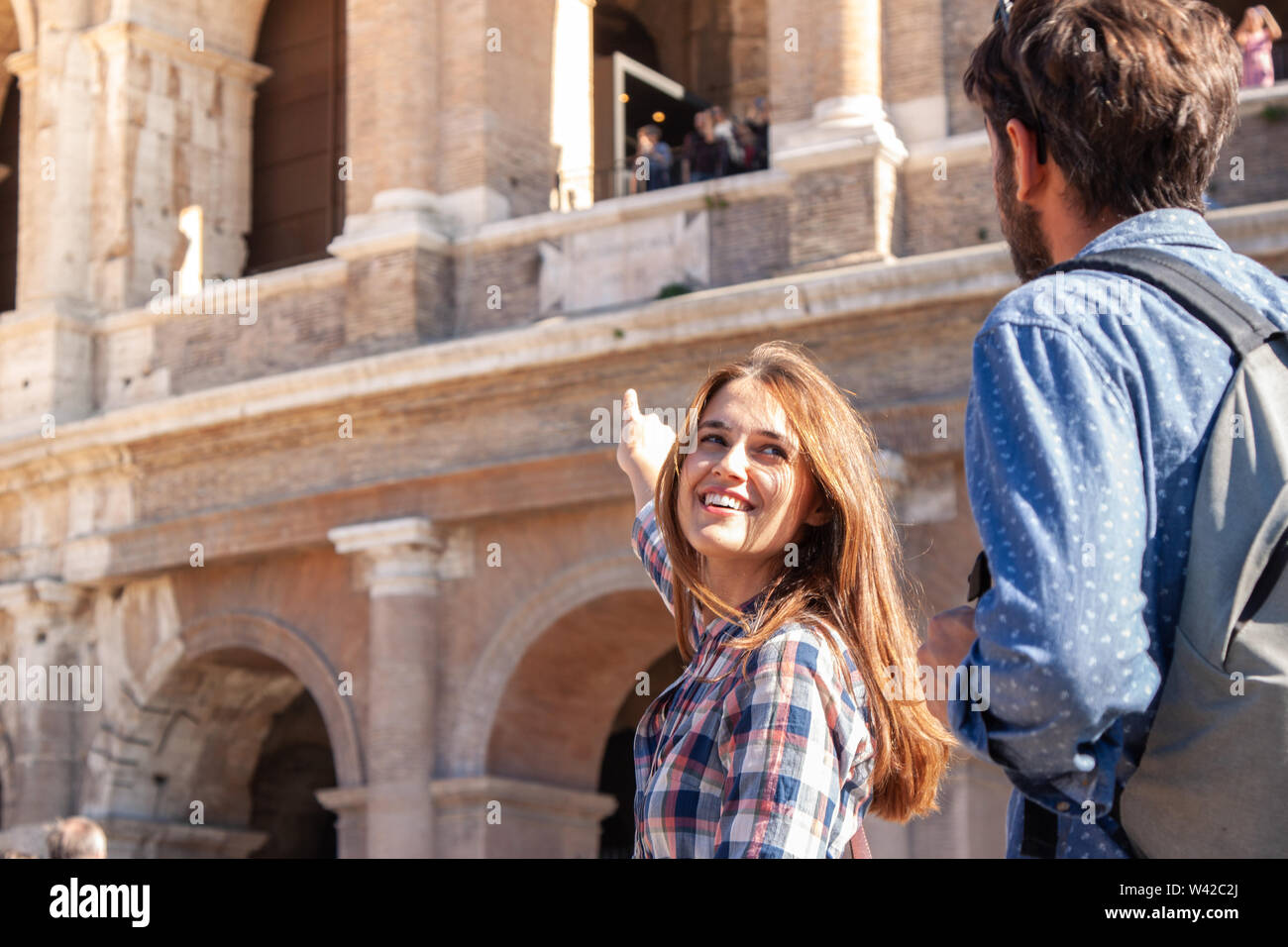 Happy young couple tourists in front of colosseum in rome pointing Stock Photo