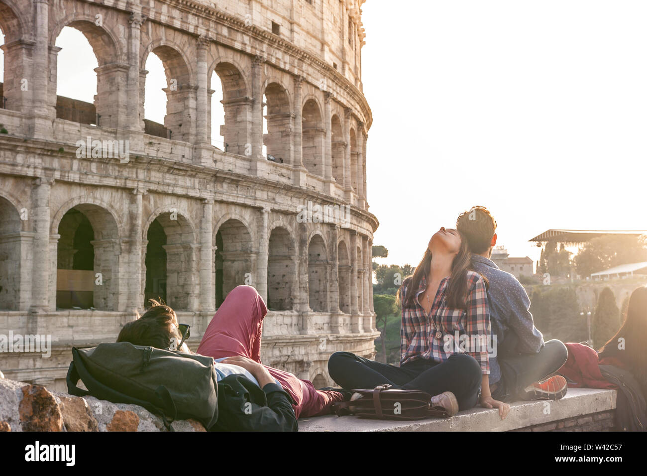 Three happy young friends sitting and lying in front of colosseum in rome Stock Photo