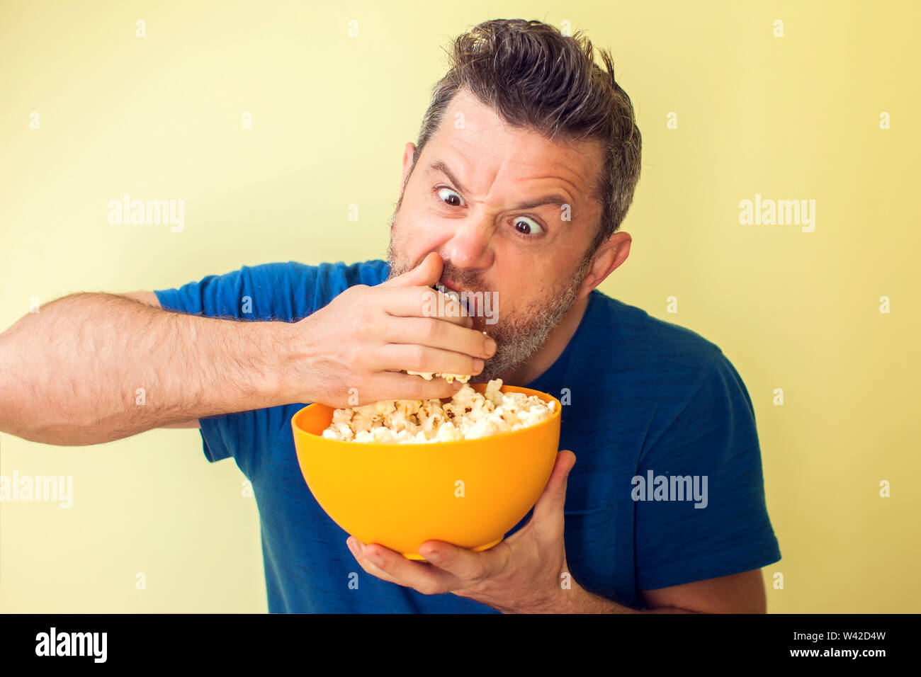 Portrait of a funny man eating popcorn over yellow background Stock Photo