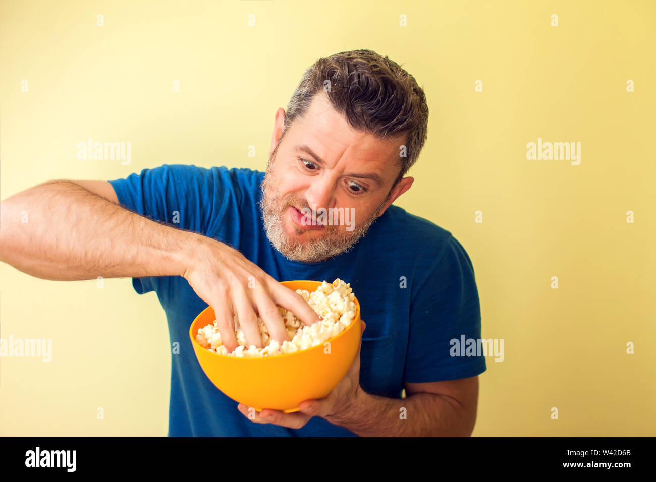 Portrait of a funny man eating popcorn over yellow background Stock Photo