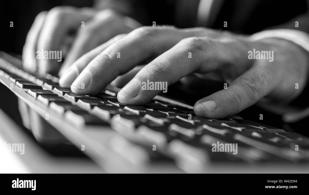 Black and white image of male hands typing on  computer keyboard. Stock Photo