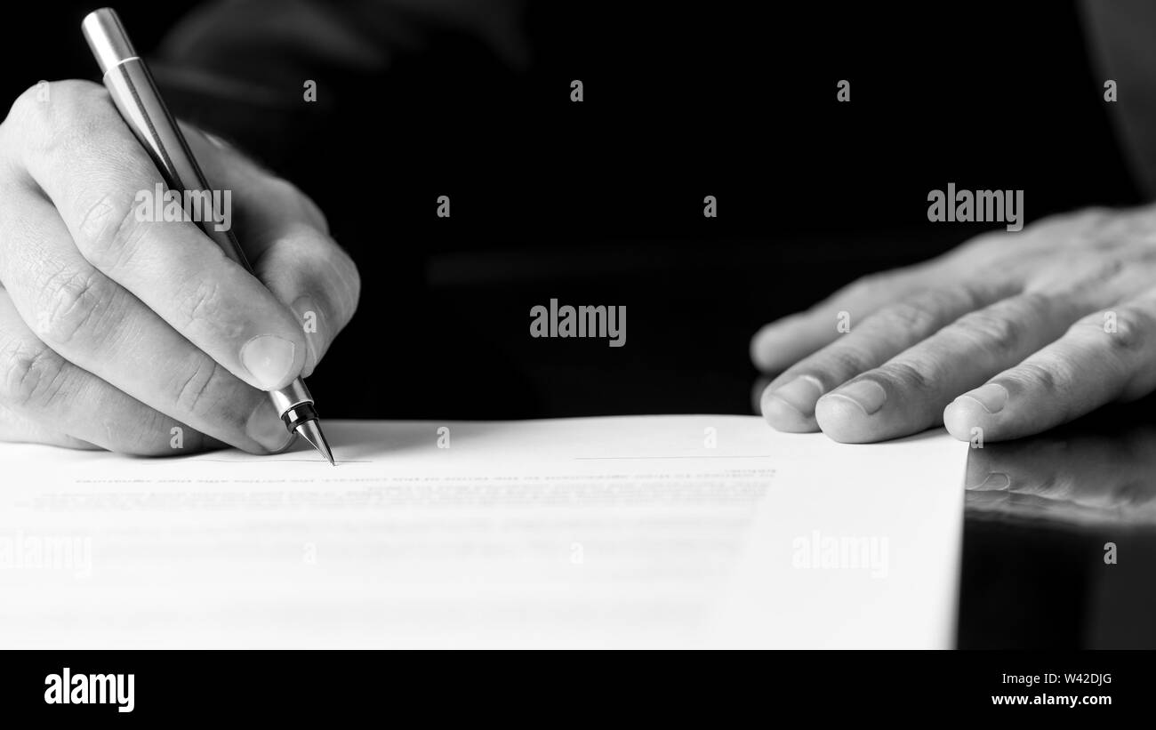 Black and white close up image of the hands of a businessman writing or signing a document with a fountain pen. Stock Photo