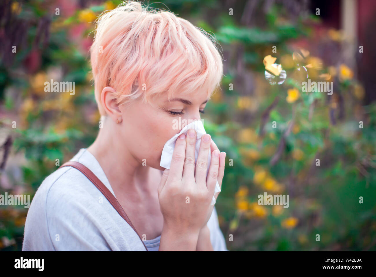 Young woman with short hair sneezing into tissue. flu, allergy, runny nose. People and healthcare concept Stock Photo