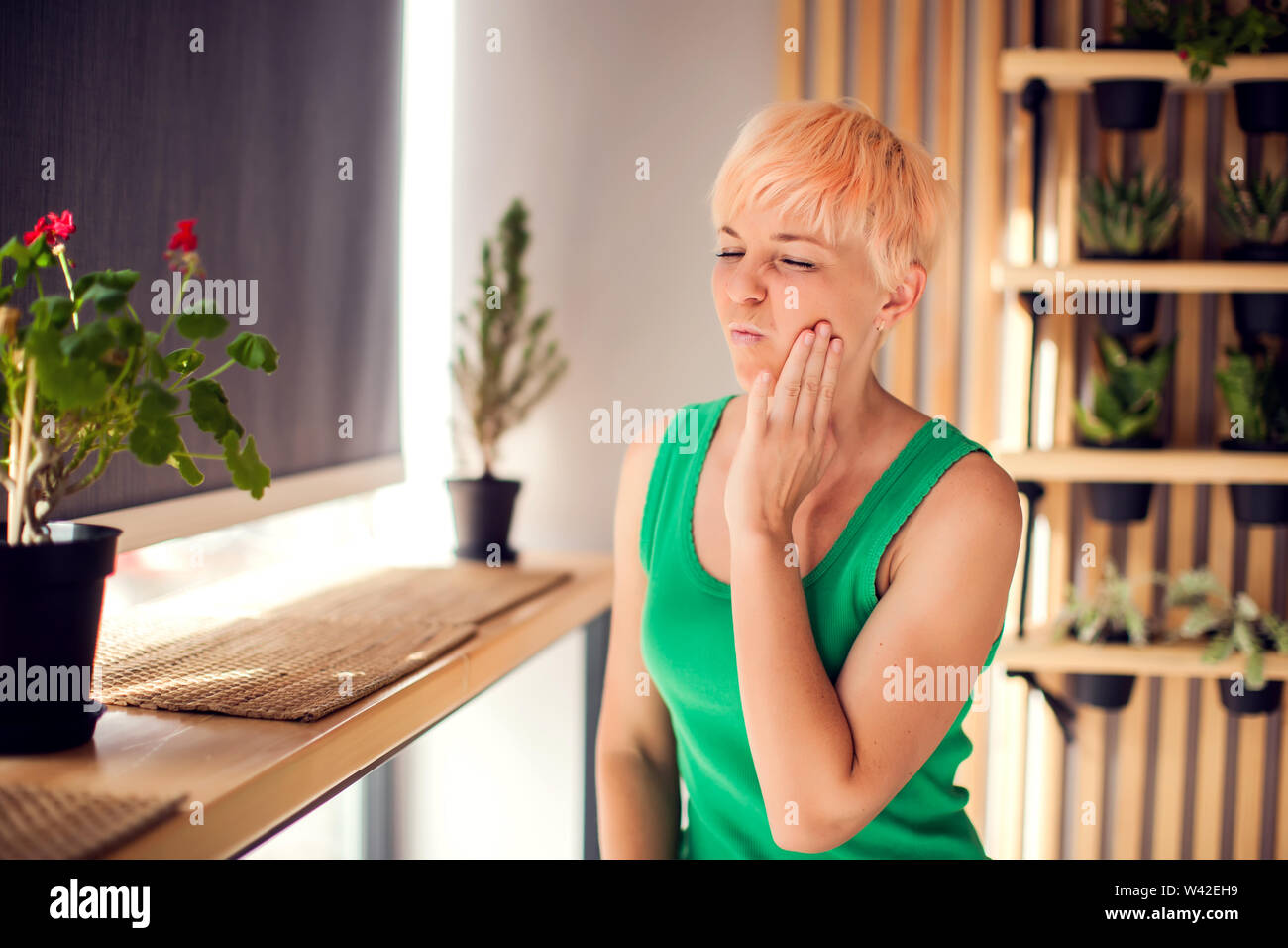 A woman with pain in her teeth is holding her face indoor. People, health care and medical concept Stock Photo