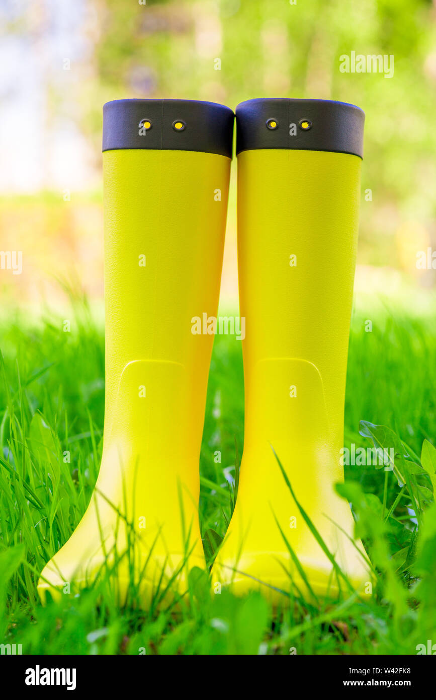 Yellow rubber boots close up on the lush green grass on the meadow ...