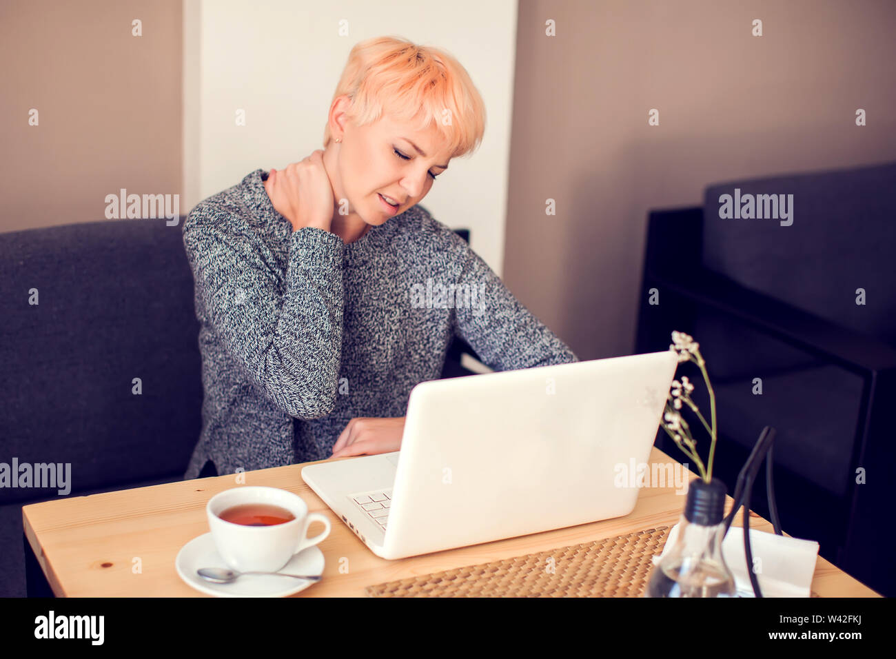 Woman feeling neck pain while working with laptop. People, health care and technology concept Stock Photo