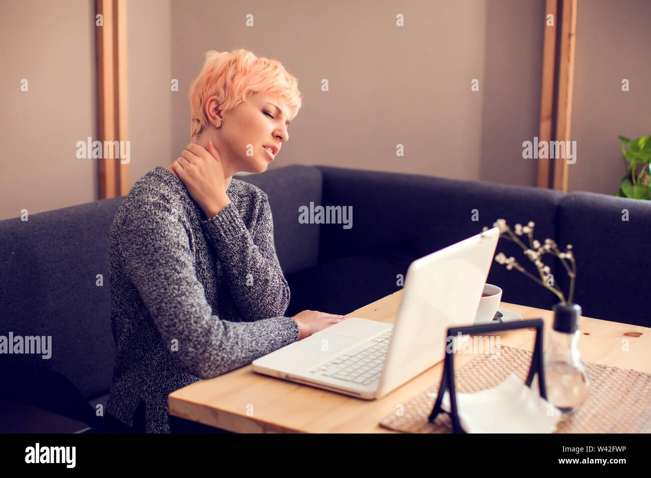 Woman feeling neck pain while working with laptop. People, health care and technology concept