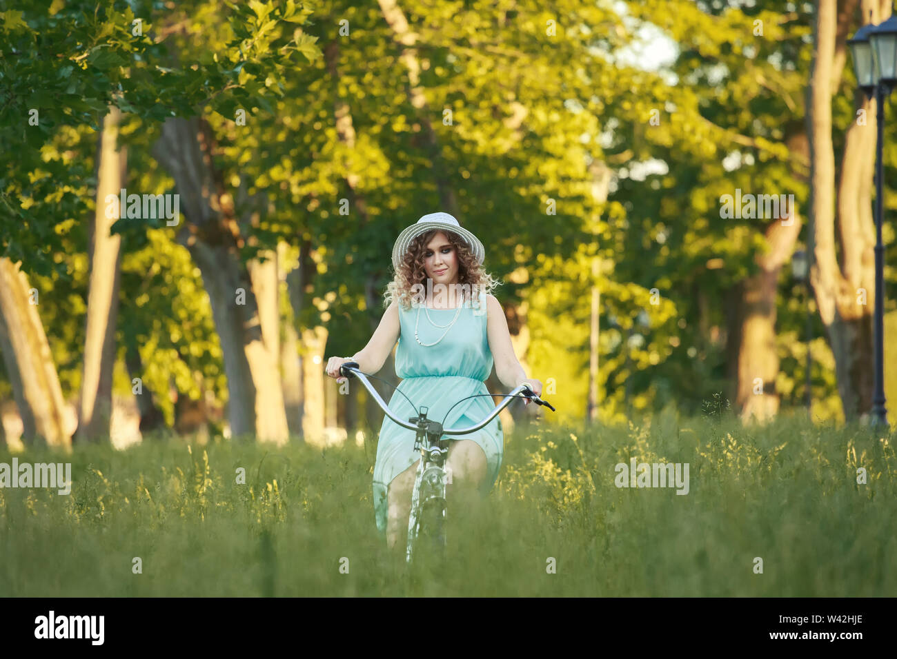 pretty woman biker on bicycle riding on green grass at sunset time Stock Photo