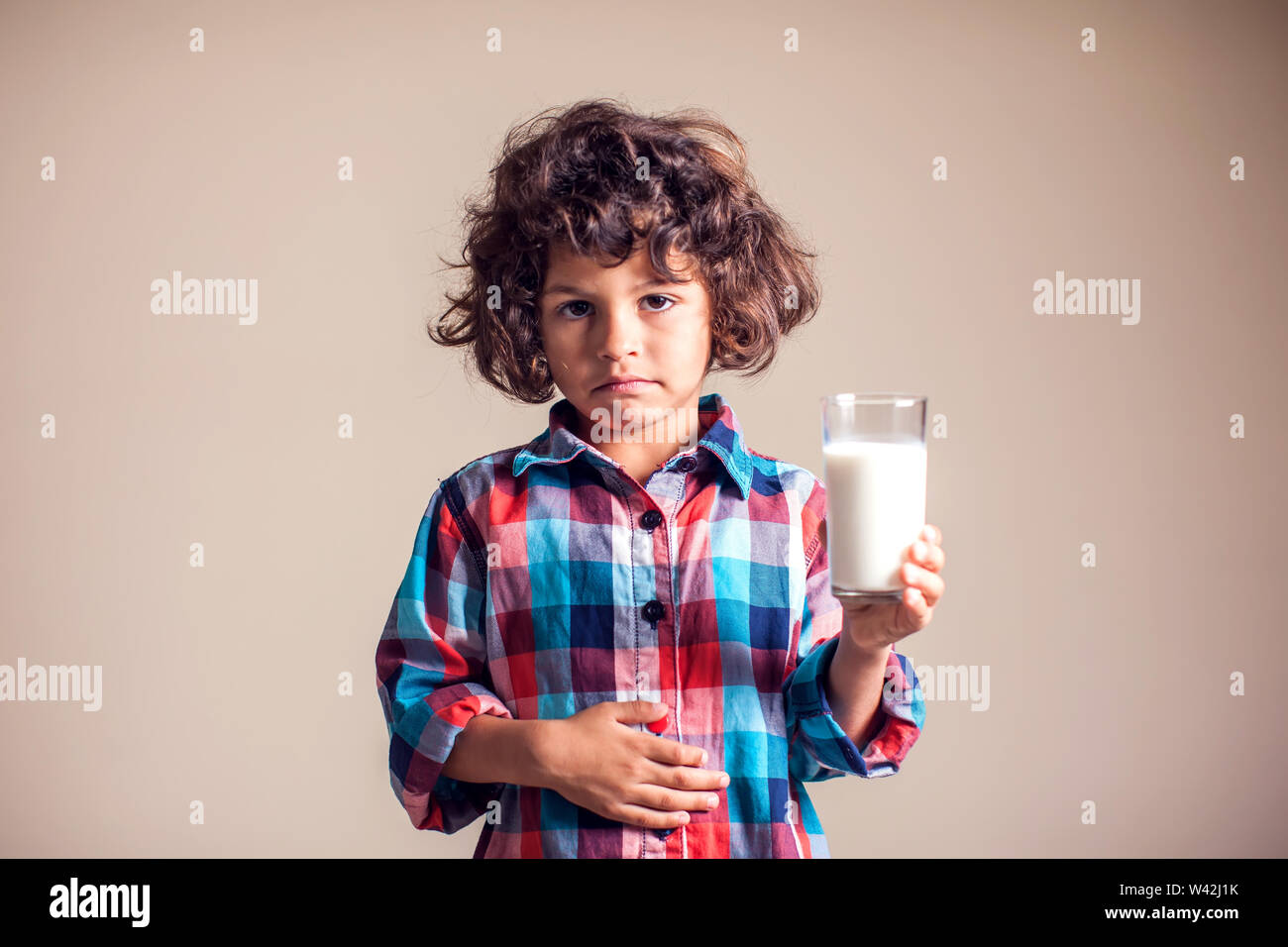 Kid boy with stomach pain holding a glass of milk. Dairy Intolerant
