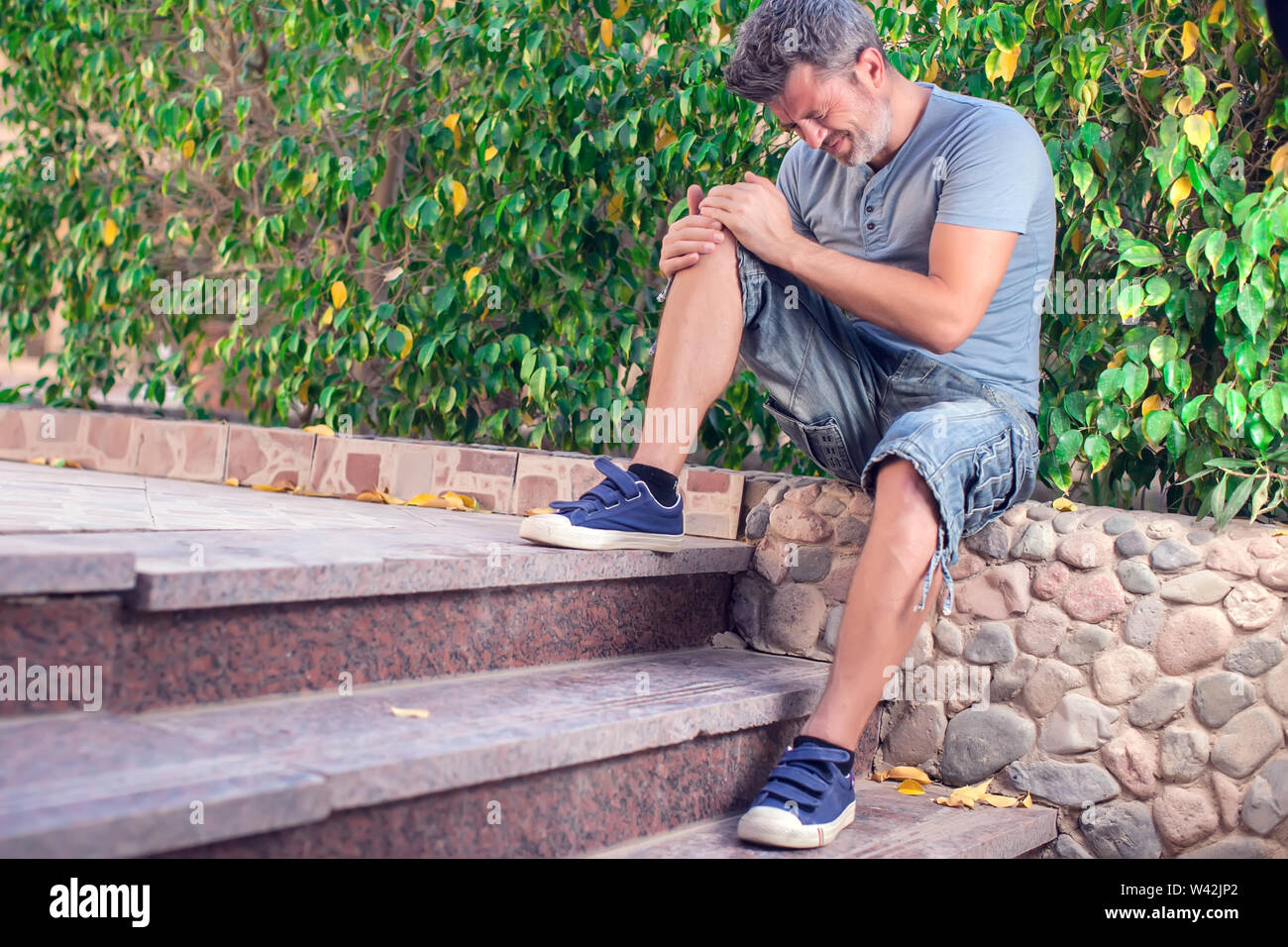 Man feels strong knee pain while walking outdoor. People, healthcare and medicine concept Stock Photo