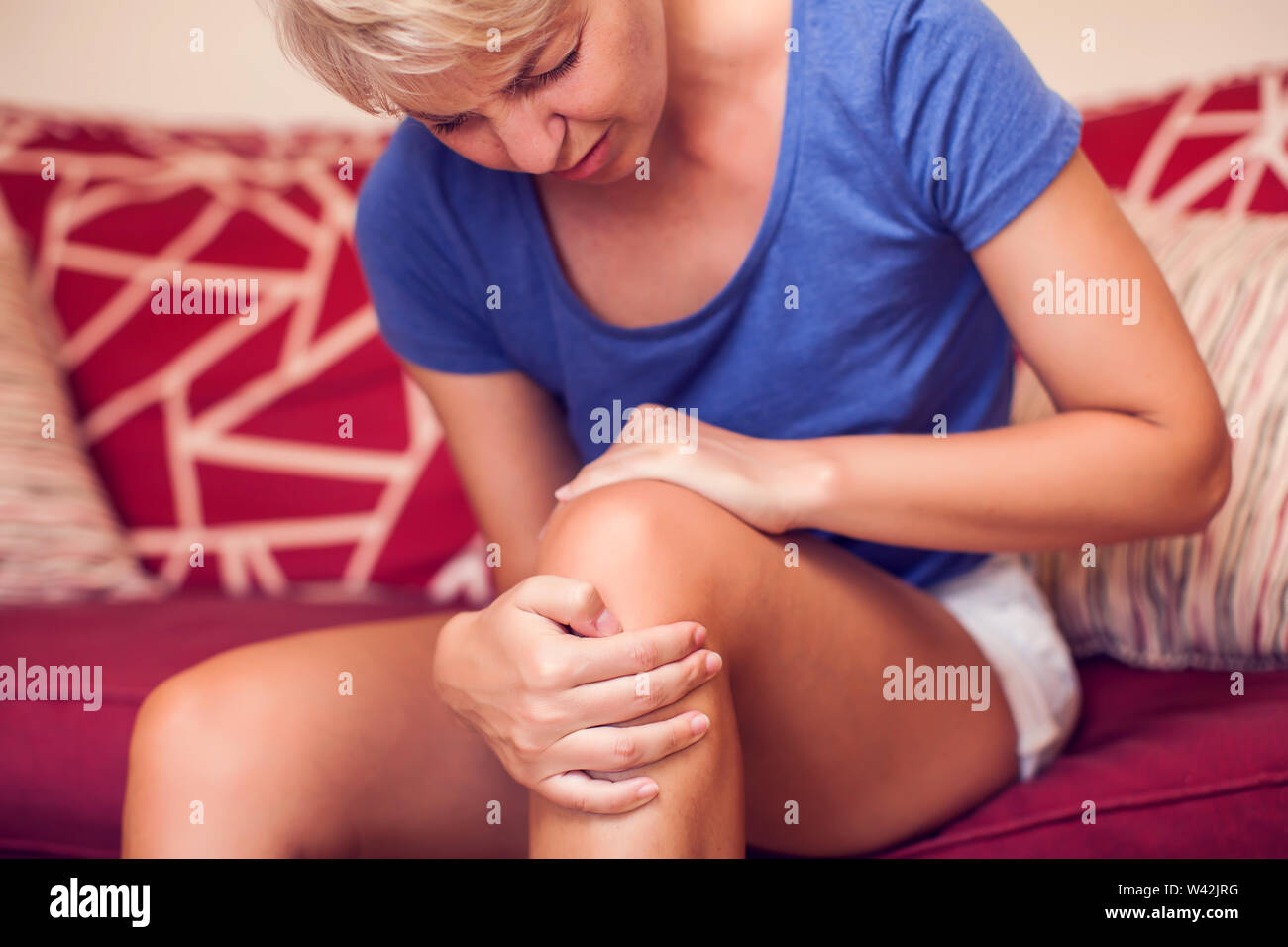 Woman with strong knee pain at home. People, medicine and healthcare concept Stock Photo