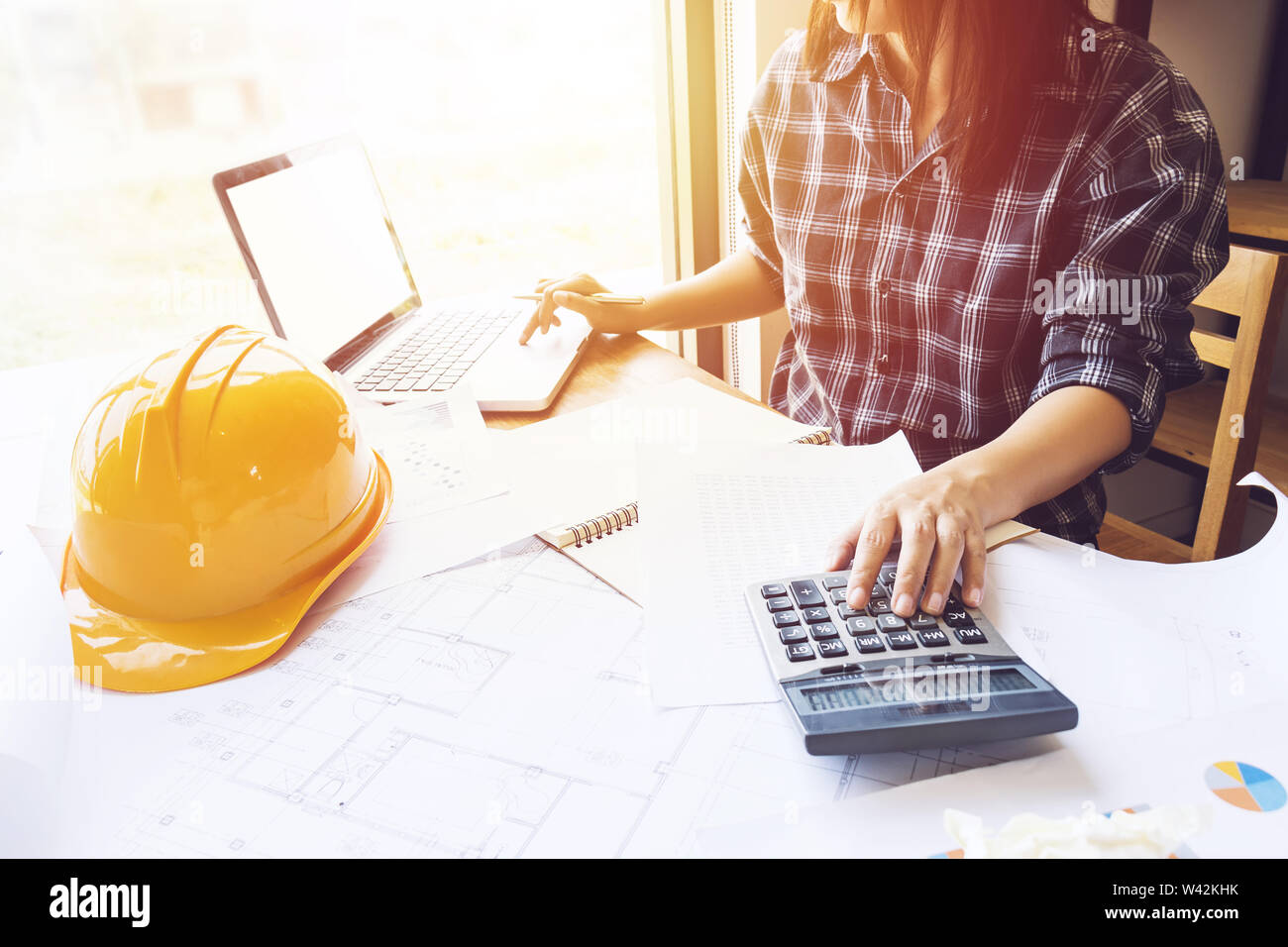 Asian engineer , architect woman using calculator for accounting and analyzing building structure from blueprint and paper chart in front of computer Stock Photo