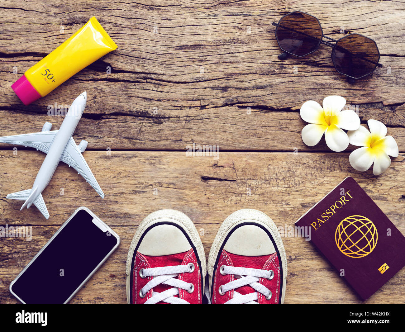 flat lay of passport , mobile , plane model , red sneakers and traveler's accessories items on wooden background with copy space. travel and vacation Stock Photo