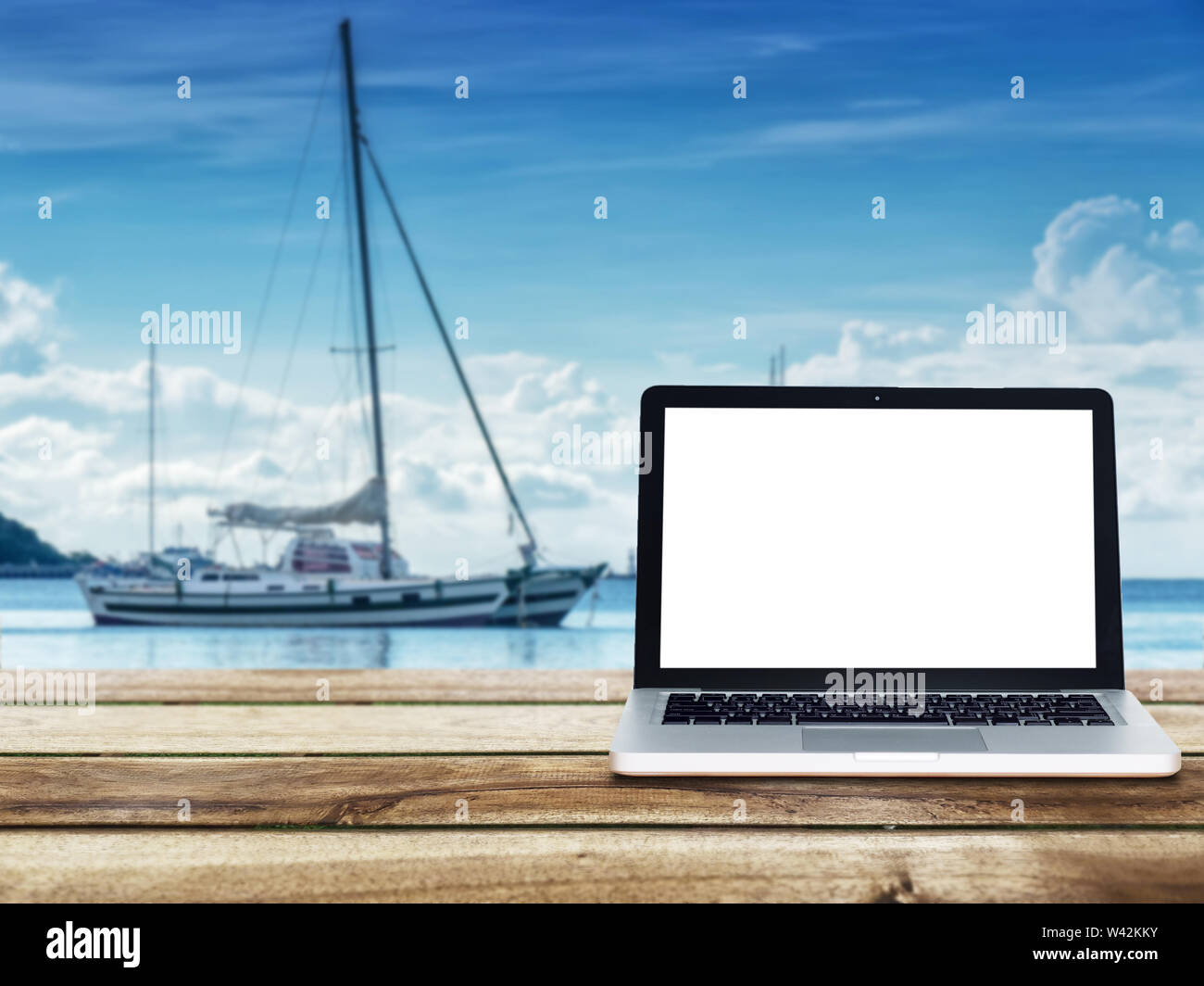 computer laptop with blank white screen on wooden table with yacht boats floating on the sea at background. Travel vacation concept. Stock Photo