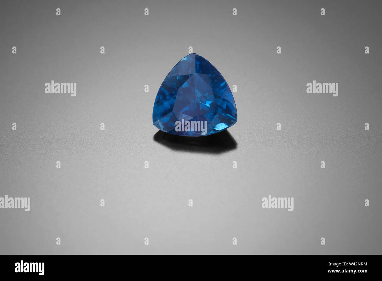 This faceted trillion cut sapphire sits on a black reflective background. Stock Photo