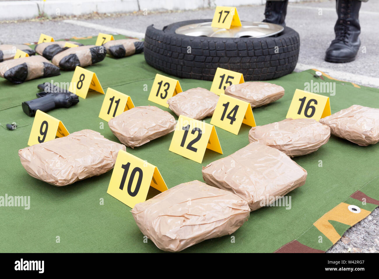 Police officer standing guard over seized packages of drug with evidence markers Stock Photo