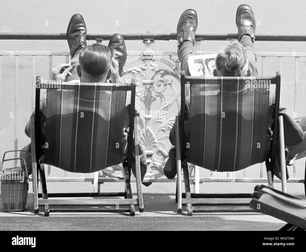 Holiday scenes at Brighton Two holidaymakers put their feet up on Brighton promenade and enjoy the sunny weather. 7th July 1963 Stock Photo