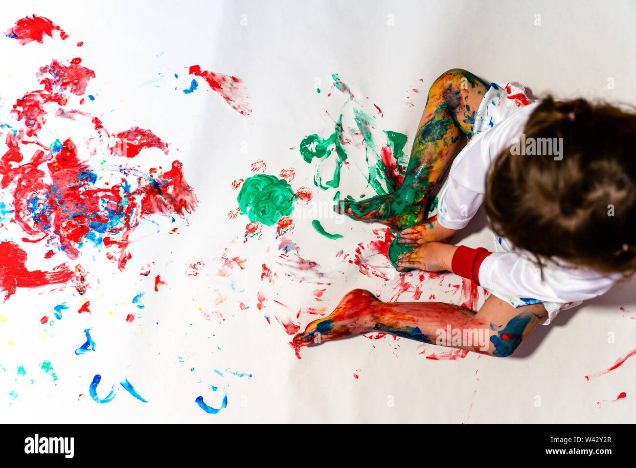 Toddler baby finger painting on a white paper on the floor Stock Photo