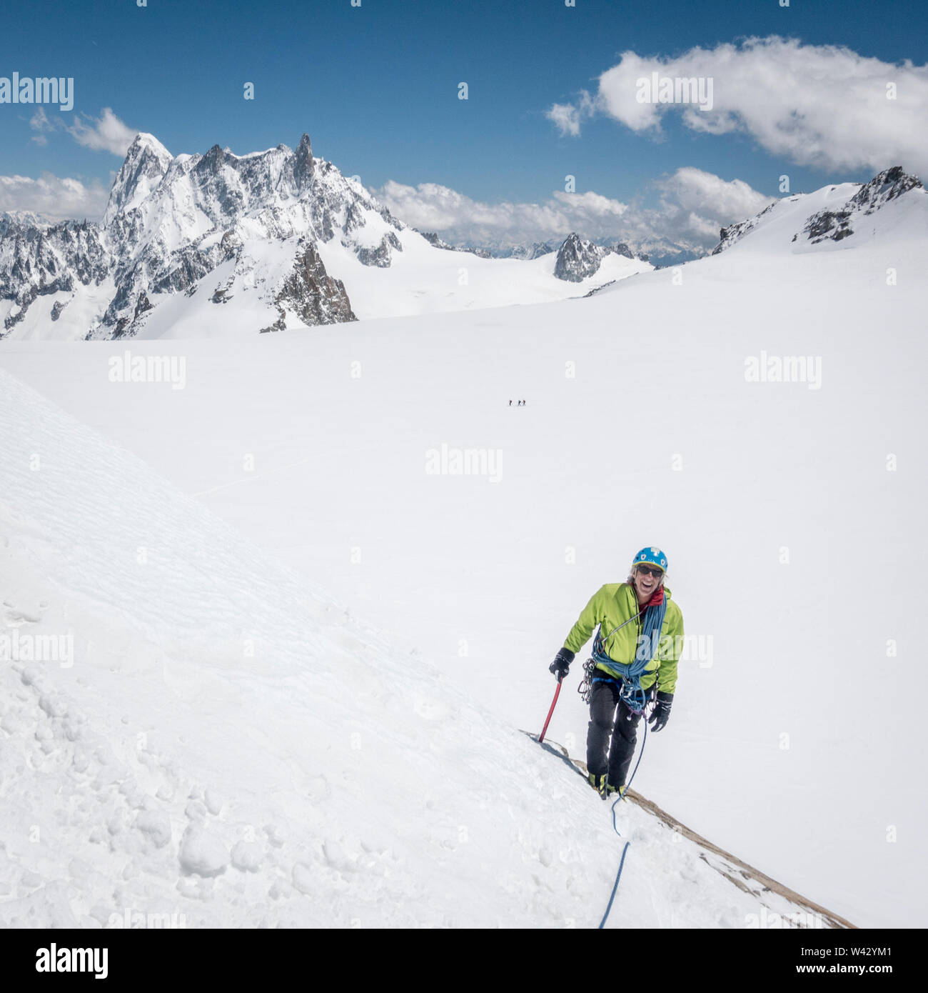A smiling mountaineer approaches a steep snow slope on a bluebird day Stock Photo