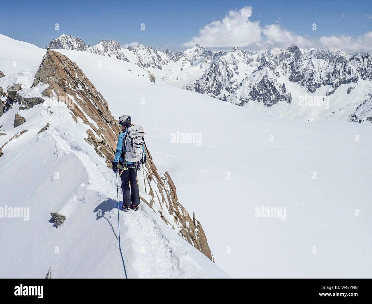 A woman mountaineer looks back from an exposed snow ridge in the Alps Stock Photo