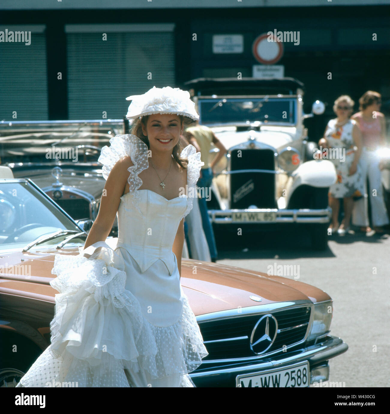 Eine junge Frau im Hochzeitskleid während einer Oldtimermesse in München in den 1980er Jahren.  A young woman in wedding dress during a vintage car fair in Munich in the 1980s. Stock Photo