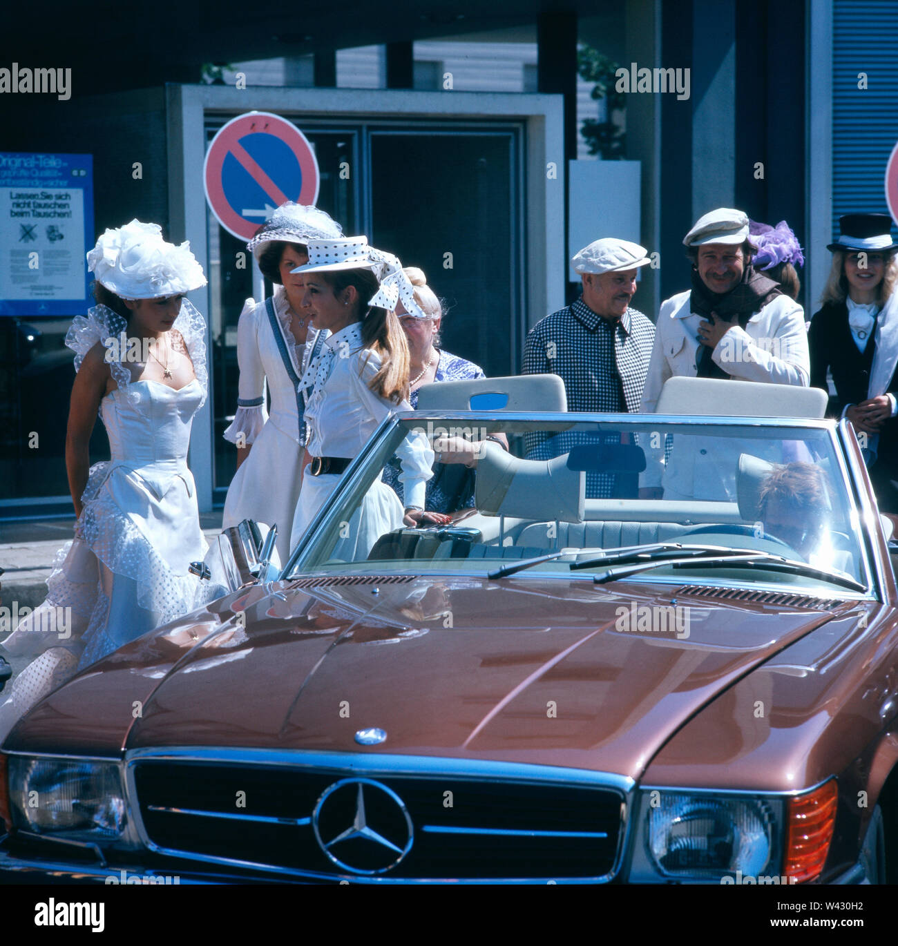 Eine Hochzeitsgesellschaft steht neben einem 1986er Mercedes-Benz 300SL Cabriolet während einer Oldtimermesse in München Ende der 1980er Jahre.  A wedding party is next to a 1986 Mercedes-Benz 300SL convertible during a vintage car show in Munich in the late 1980s. Stock Photo