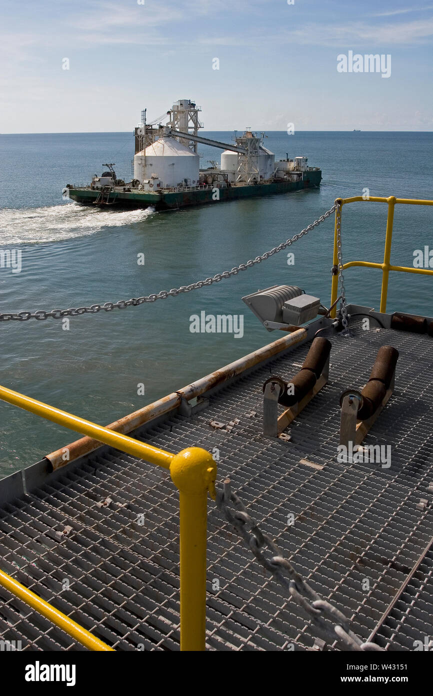 Mining, managing & transporting of titanium mineral sands. Barge leaving port to discharge product into OGV at sea &  showing jetty infrastructure . Stock Photo