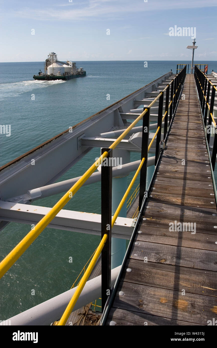 Mining, managing & transporting of titanium mineral sands. Barge leaving port to discharge product into OGV at sea &  showing jetty infrastructure . Stock Photo